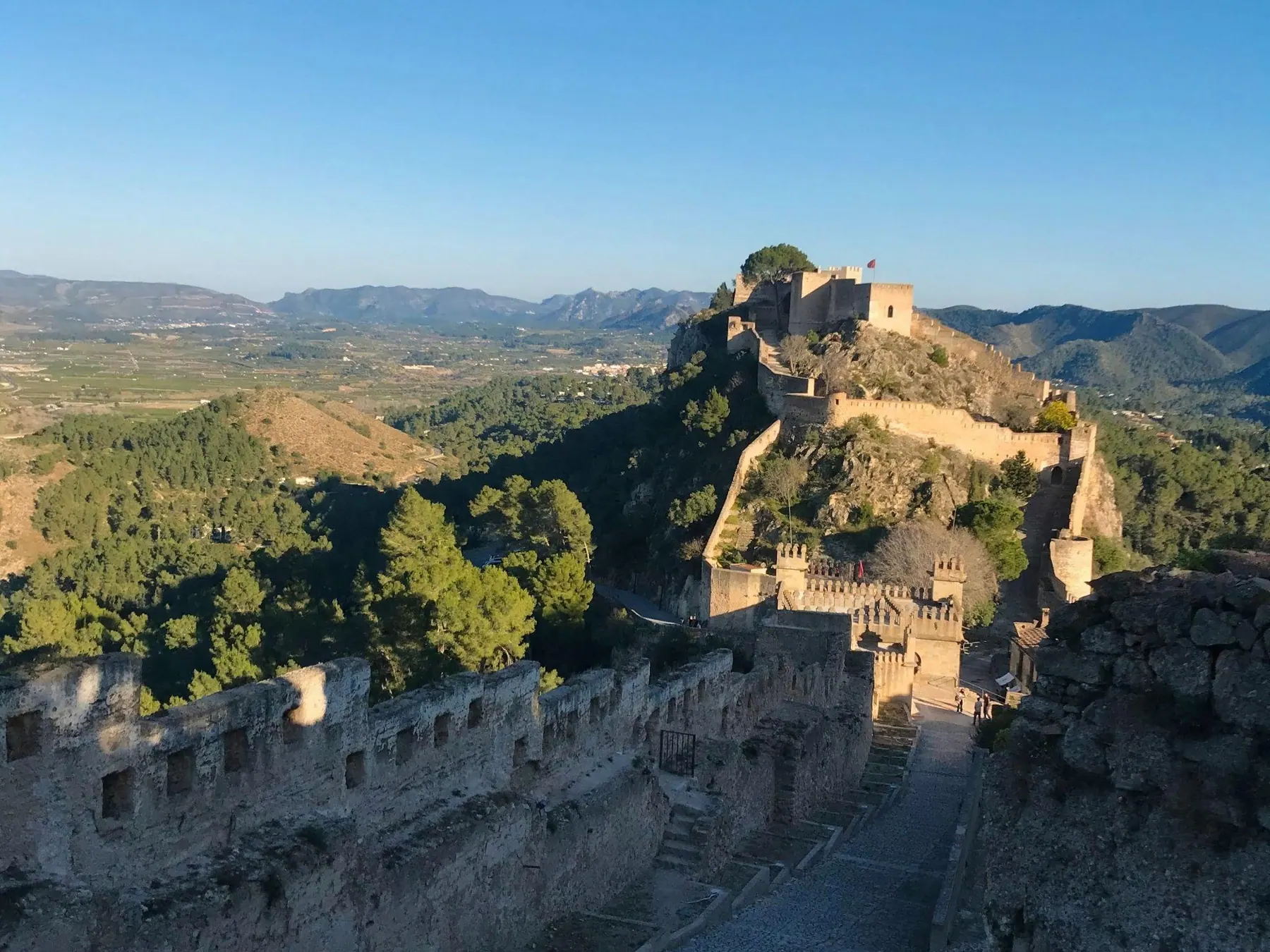 Fortified stone ramparts and watchtowers of Xàtiva Castle looking over the green valley below