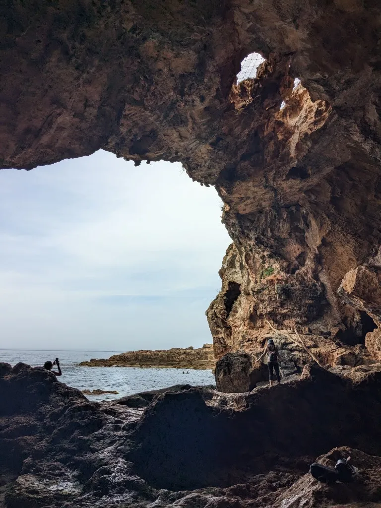 Sunlight illuminating the vast sea-carved limestone arch of Cova Tallada opening out to the turquoise sea
