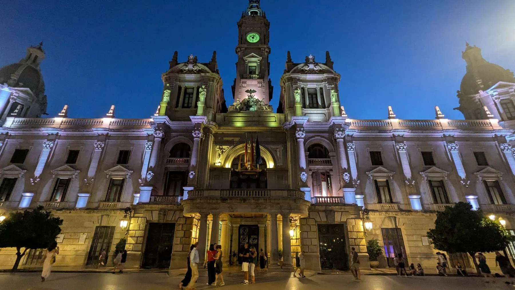 Fachada clasicista y torre del reloj del Ayuntamiento de Valencia iluminadas al anochecer frente a la Plaza del Ayuntamiento