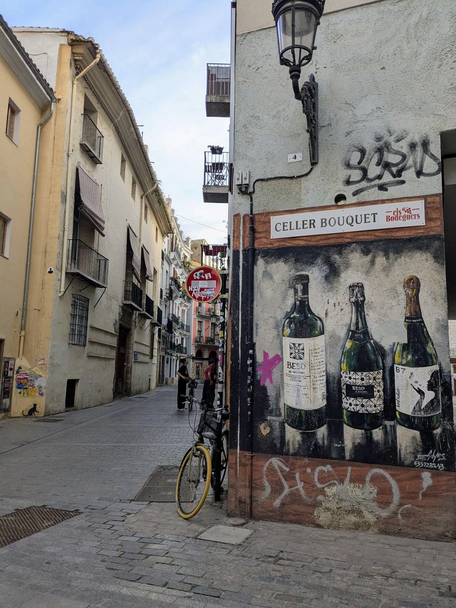 Callejón en El Carmen con mural de botellas de vino en la pared, bicicleta y arte urbano