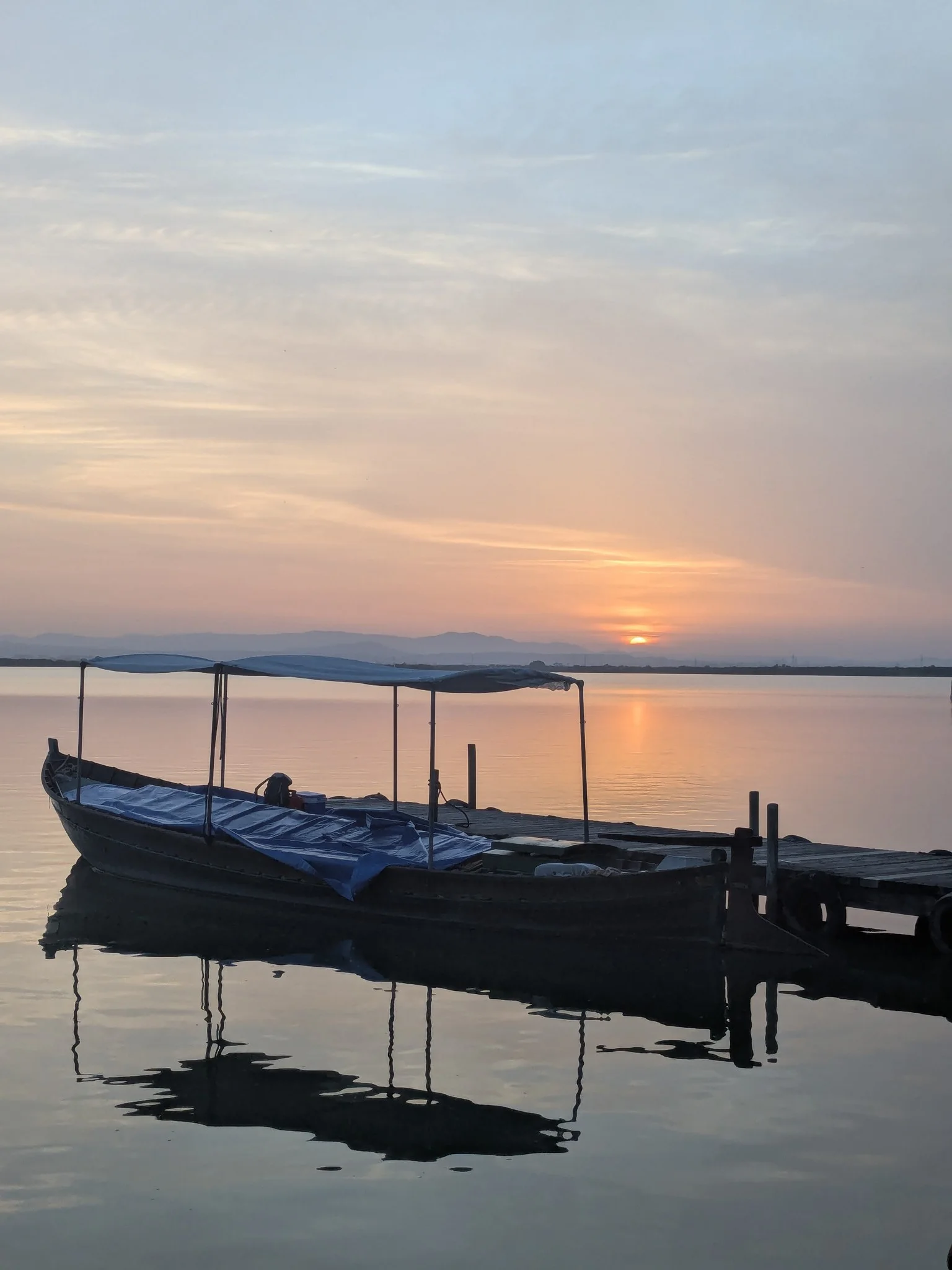 Barca tradicional de madera amarrada a un embarcadero rústico en las aguas tranquilas del lago de la Albufera al atardecer