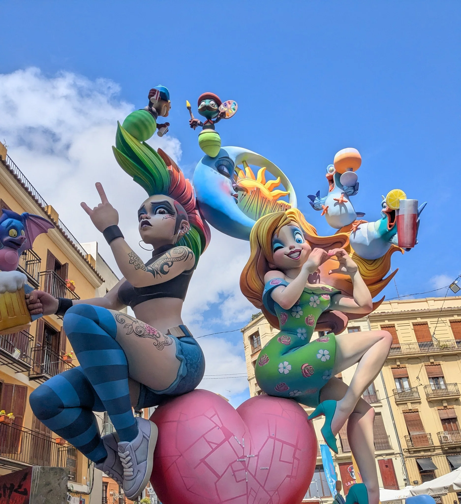 Monumento de falla monumental y colorido con figuras satíricas sobre un corazón rosa en las calles de Valencia durante las Fallas