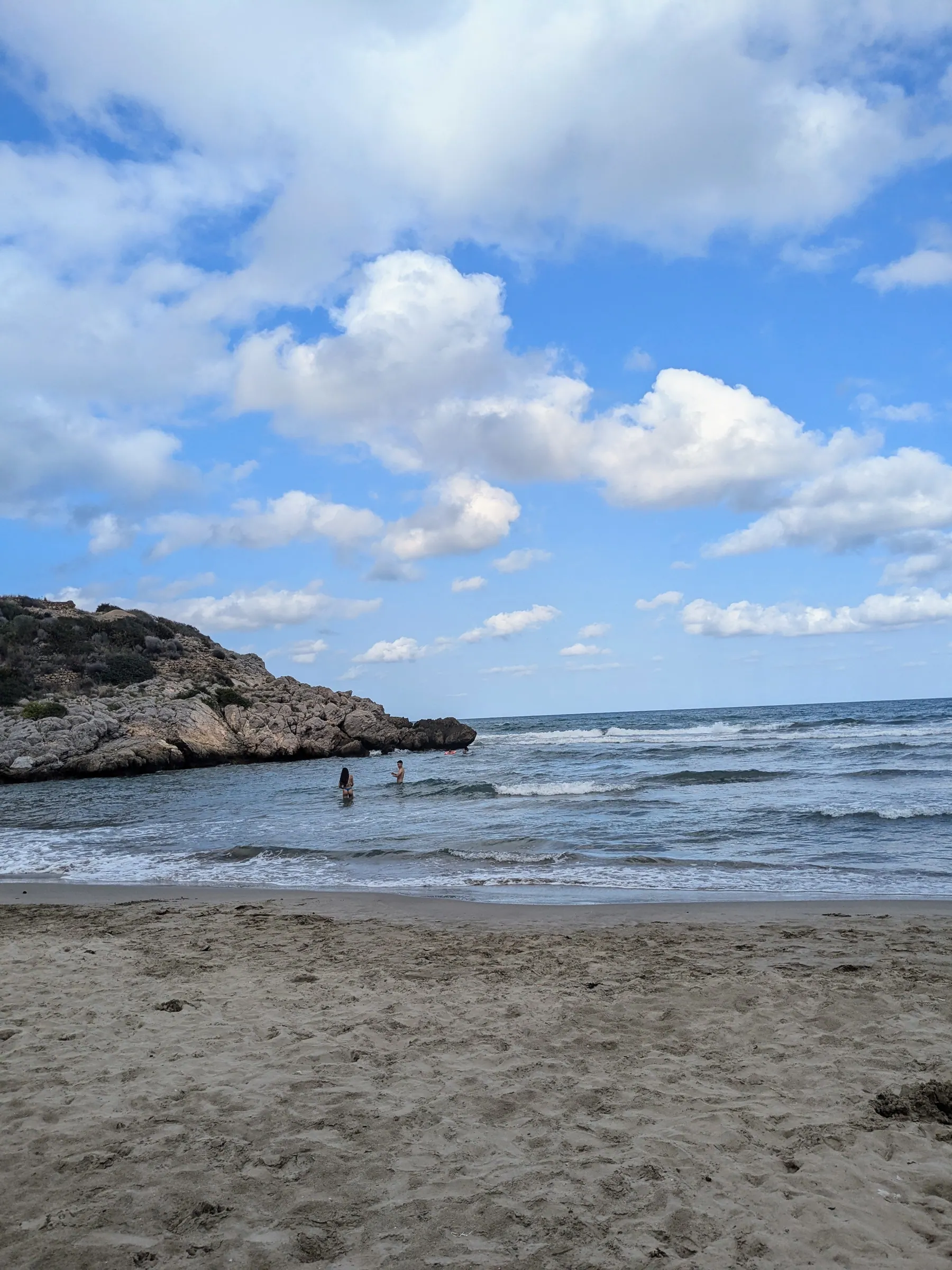 People swimming beside the sandy beach and rocky cove at Cala Retor near the Vía Verde del Mar